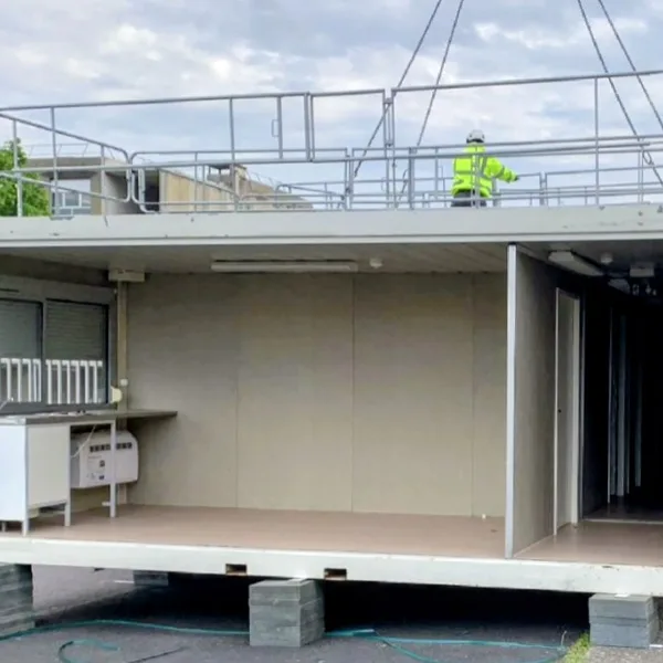 Modular container cabin being craned onto stacks of recycled-plastic corner pads