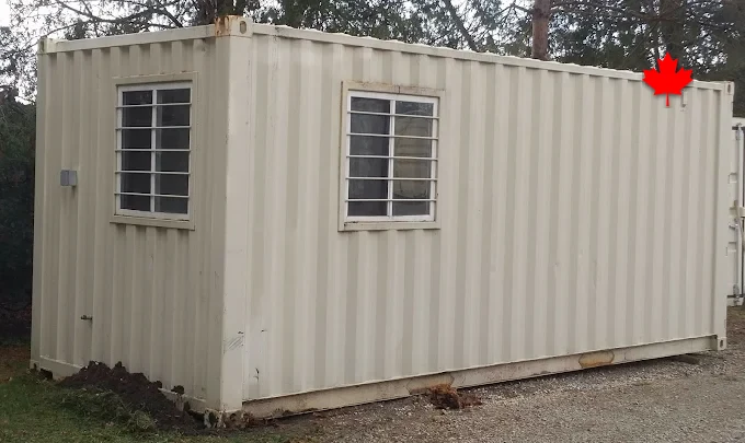 Cream site office container with two barred windows beside the tree line