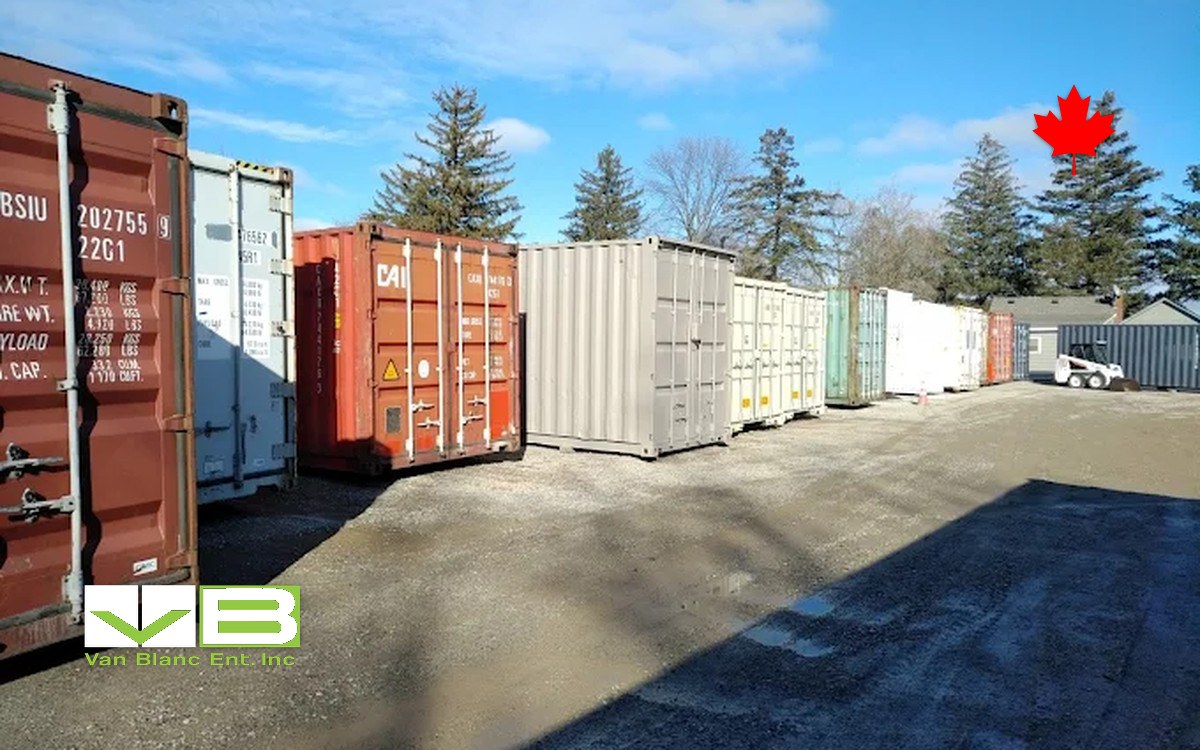A row of containers on gravel with doors facing the lane for inspection