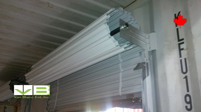 Shop crew fitting a new roll-up door assembly to a container opening.