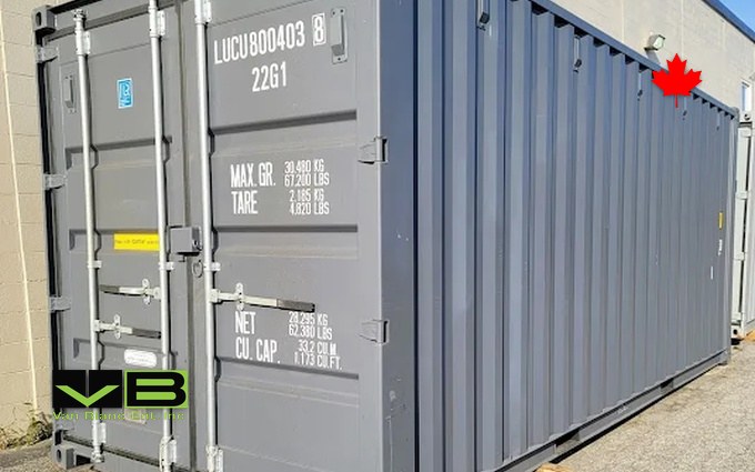 A grey one-trip twenty-footer parked tight along a block wall, data plate crisp, doors still glossy.
