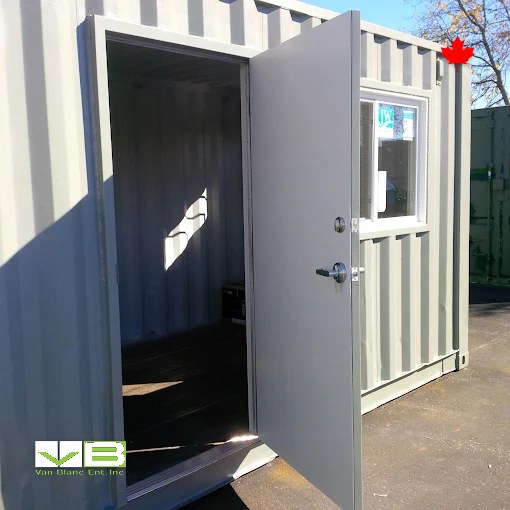 Grey unit with its personnel door swung open and a framed window, set up as a site room.