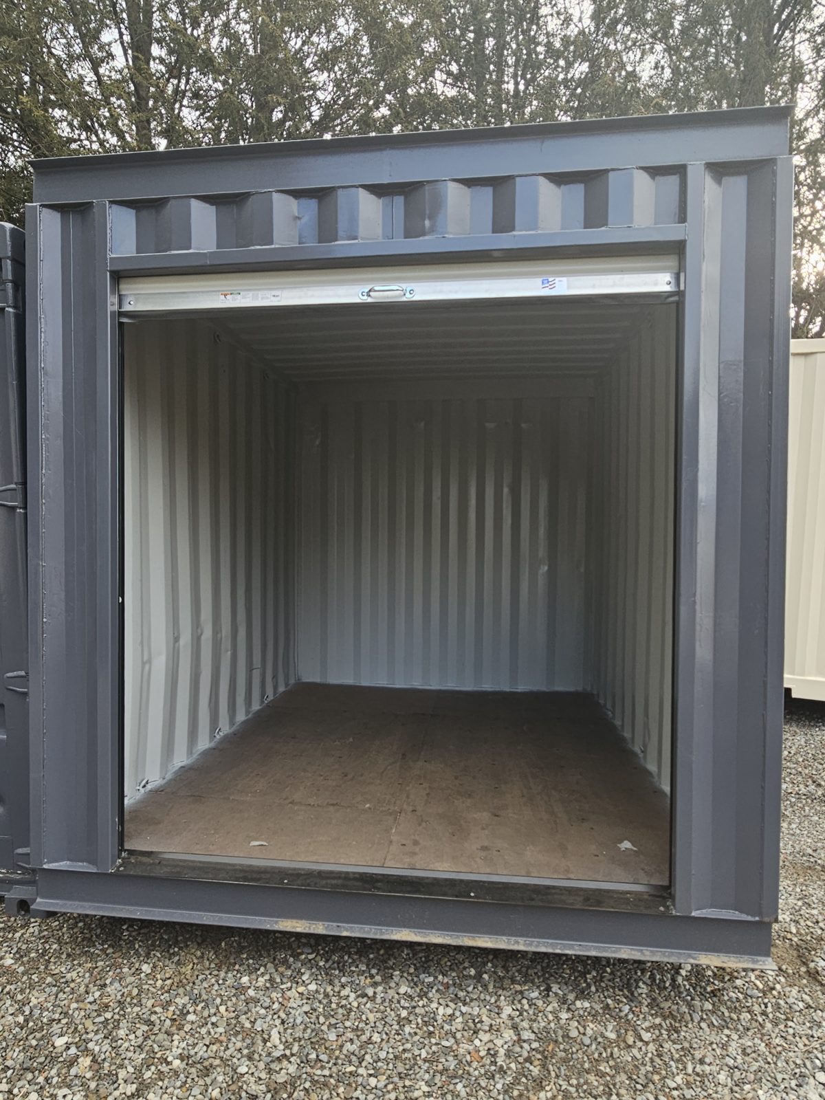 Charcoal 10ft container with its white roll-up door raised, showing a painted white interior, a wood floor and the steel sill across the opening
