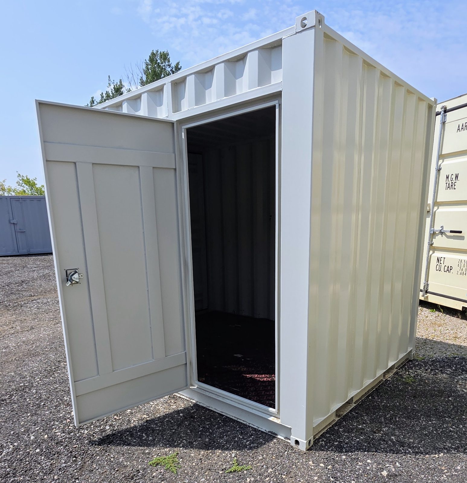 Light grey 10ft on a gravel lot with its side man door swung wide open to a dark interior