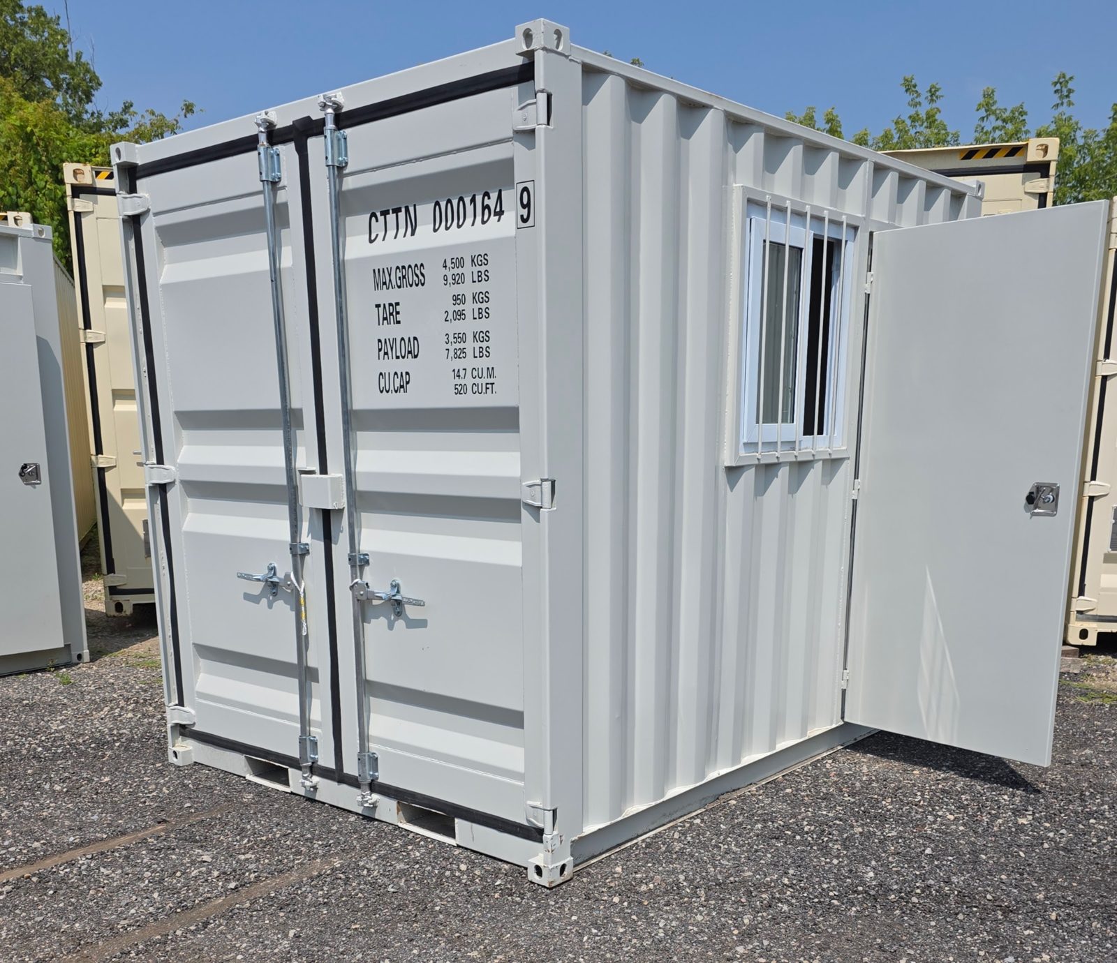 Light grey 10ft with closed cargo doors, a barred side window and an open man door, parked on a gravel lot under a blue sky