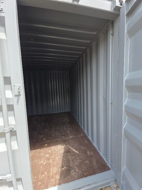One cargo door swung open on a 12ft container, showing light grey painted walls and roof, a corrugated far wall and a scuffed brown wood floor