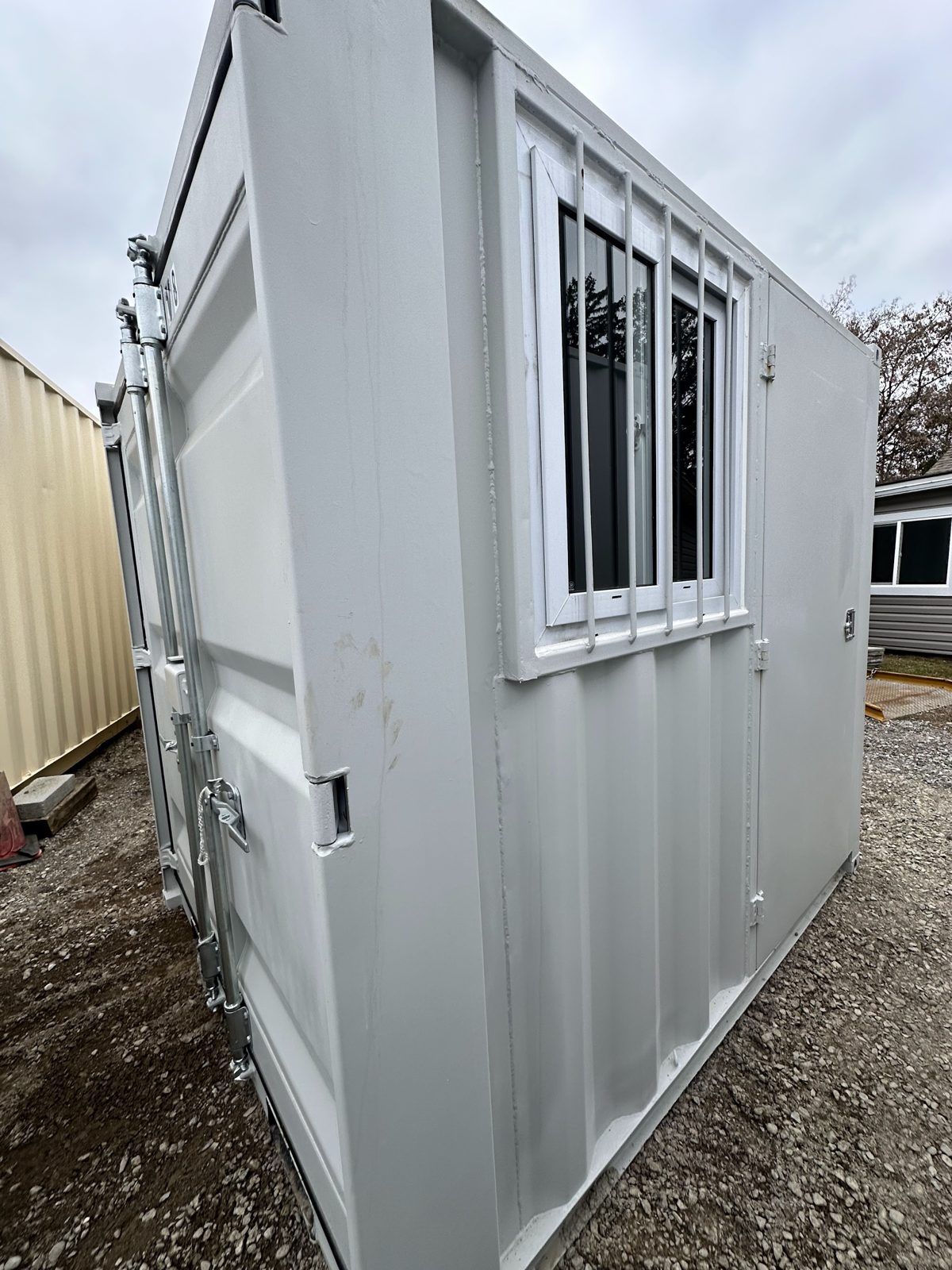 Wide-angle view of a grey 8 foot container with cargo doors on its end and a man door beside a barred window on the side wall