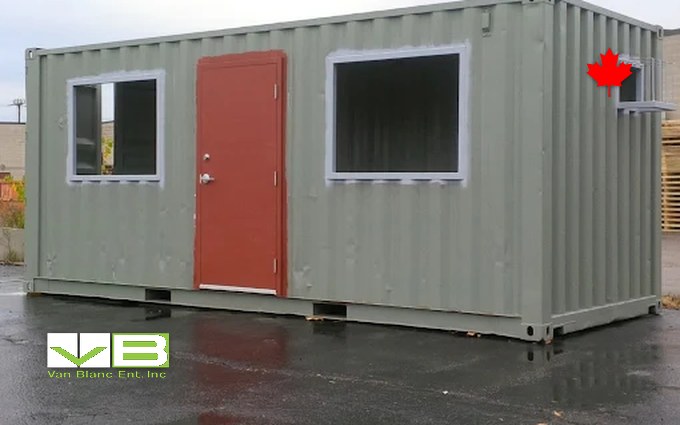 A converted shipping container with a red steel man door and a window, the small shop or office that arrives built beside a rigid-frame kit