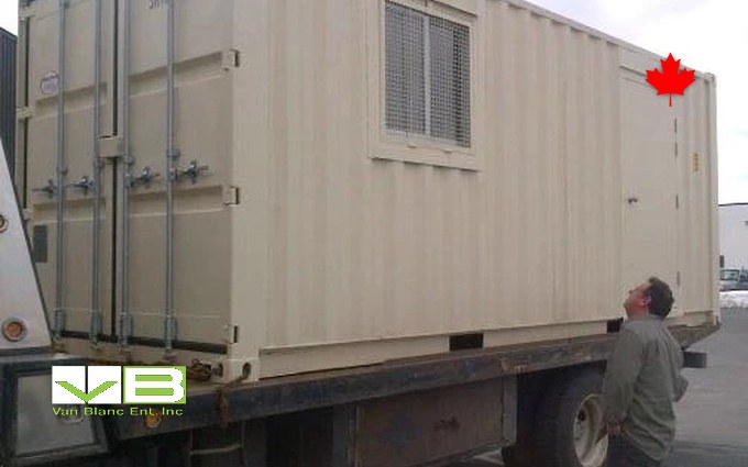 A cream converted unit with window and man door riding a flatbed, the delivery crew looking it over.