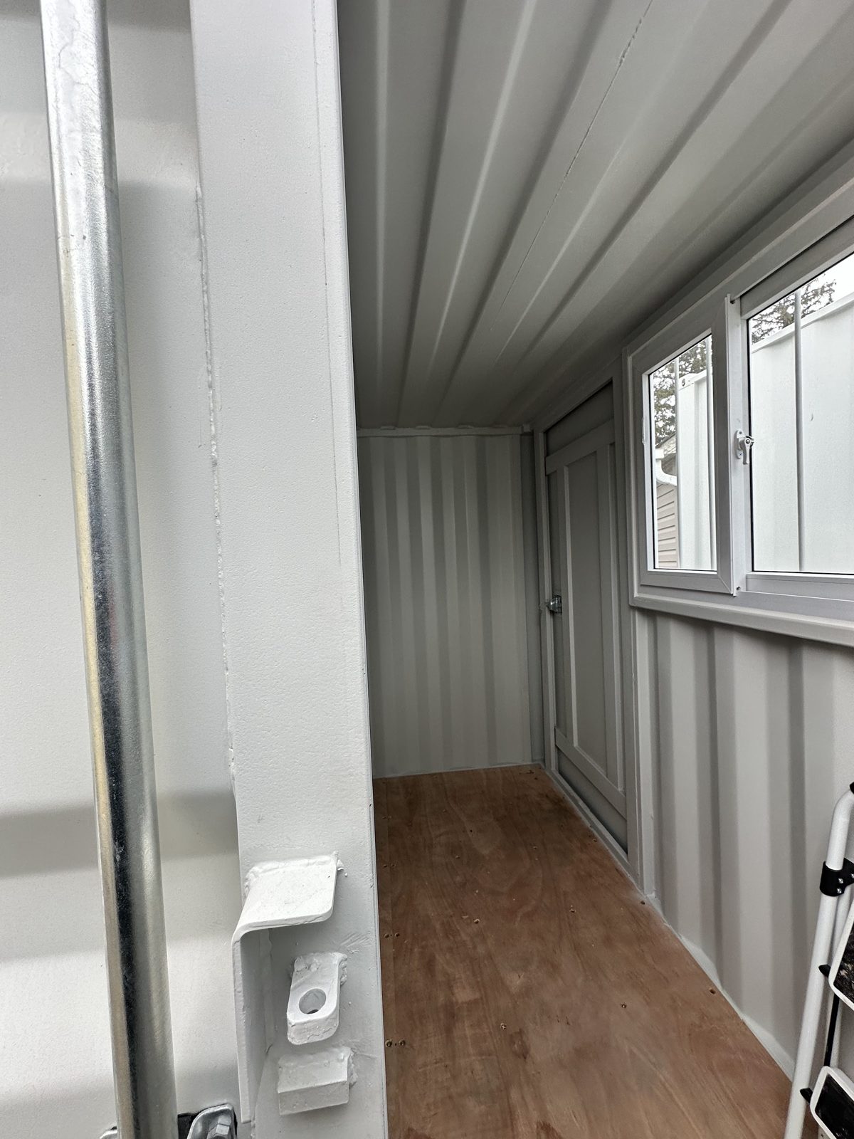 View through the cargo doors of an 8ft: bare plywood floor, light grey painted walls and ceiling, and a window and man door on the right-hand wall