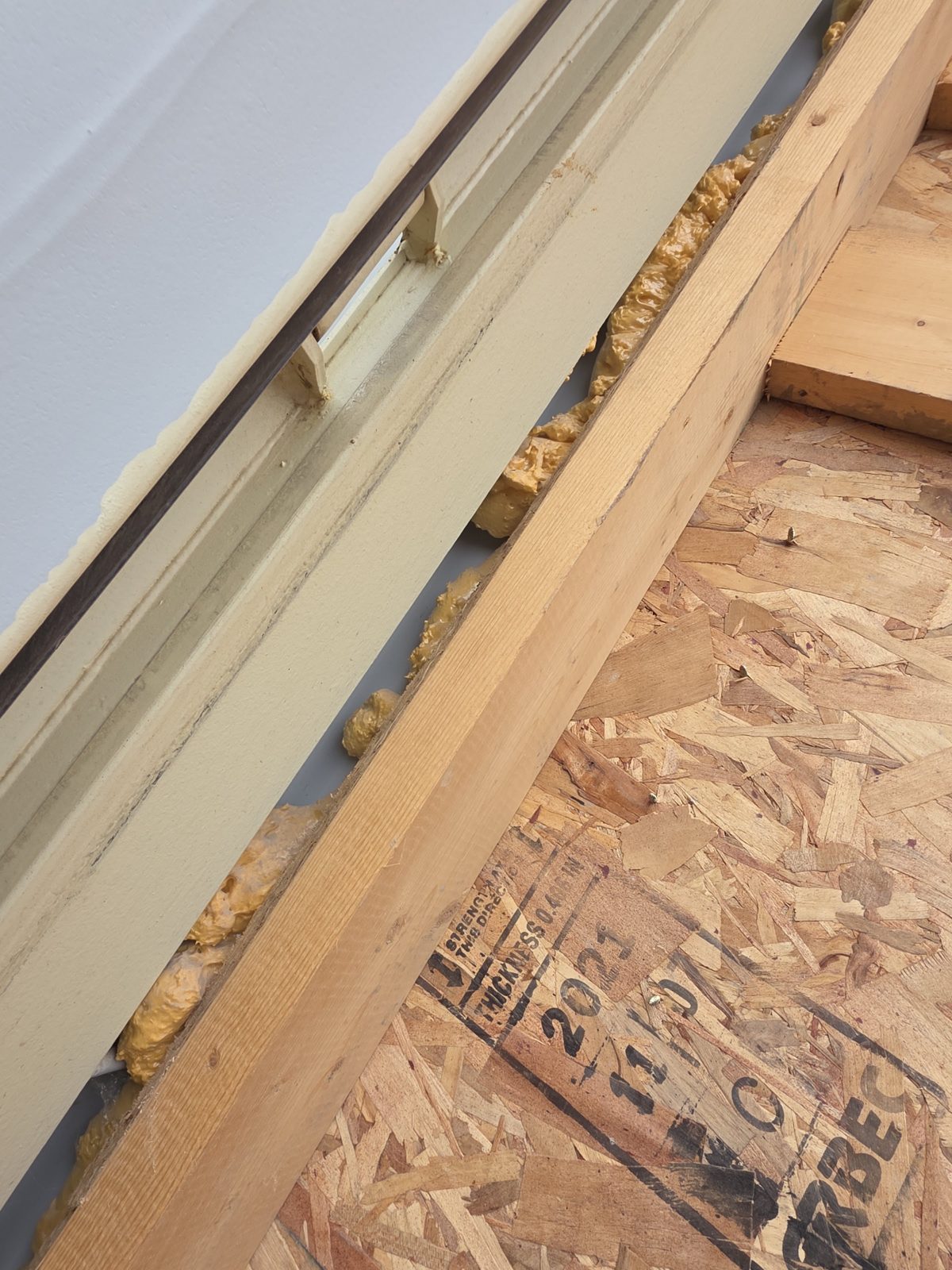 Wood framing set tight against the steel door frame of an insulated container, amber foam squeezed into the gap and an OSB sheet beside it