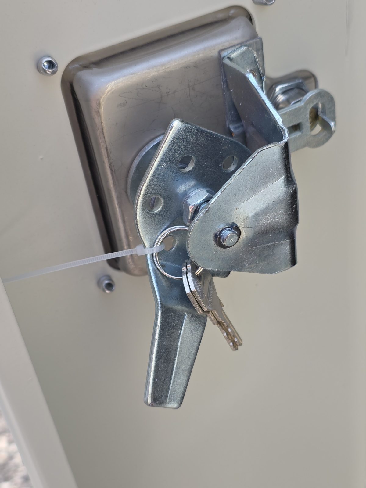 Recessed steel handle on the man door of a light grey 10ft, with a padlock hasp and a pair of keys tied on with a cable tie