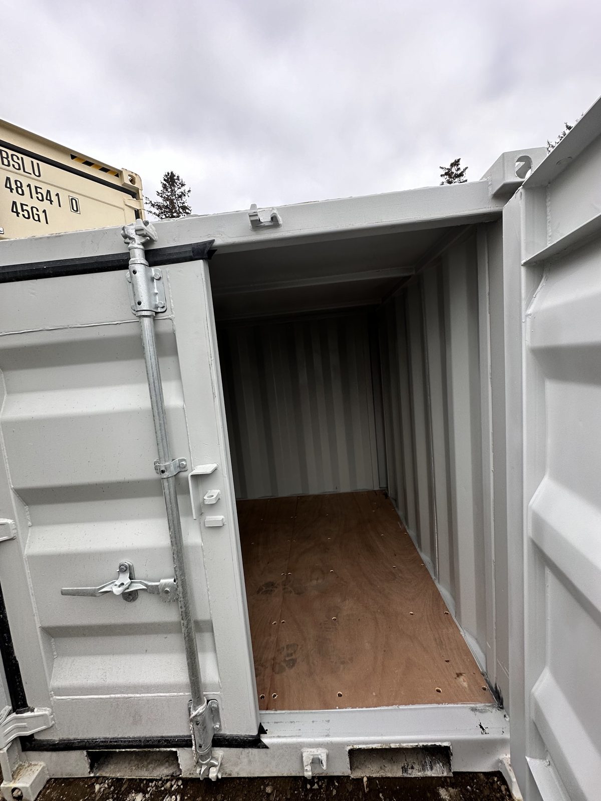 Open cargo door on a grey 6 1/2 ft mini showing a plywood floor, painted corrugated walls and fork pockets below the door sill
