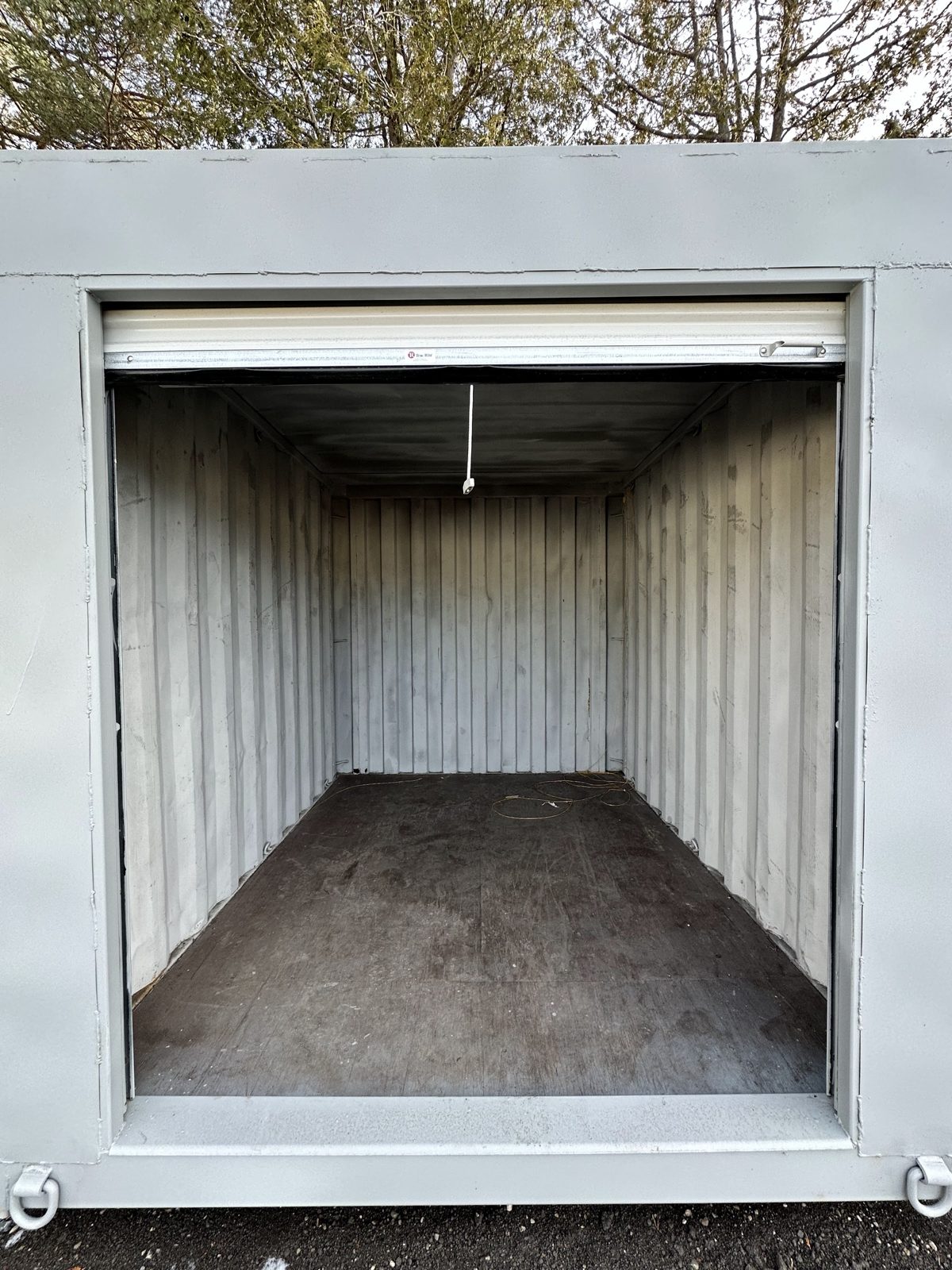 White roll-up door raised into its coil under the header of a light grey 10ft, with an empty painted interior, a dark floor and a flat steel sill across the bottom of the opening