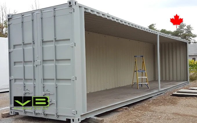 A grey open-side forty-footer with its long wall removed, stepladder standing inside the primed shell.