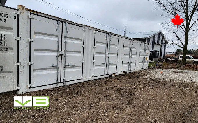 A white open-side container with its full run of side doors closed, staged on a rural commercial site