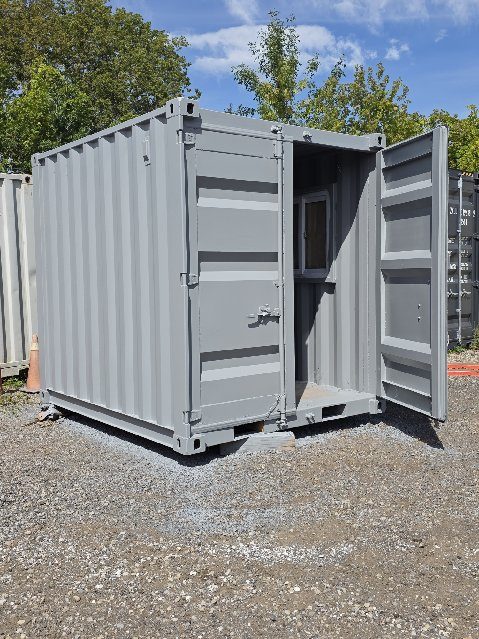 Repainted grey 9ft on fresh gravel with its right cargo door swung open, showing a window frame inside and a plywood floor