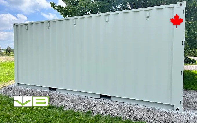 A pale one-trip unit set on a fresh gravel pad at the grassy edge of a property