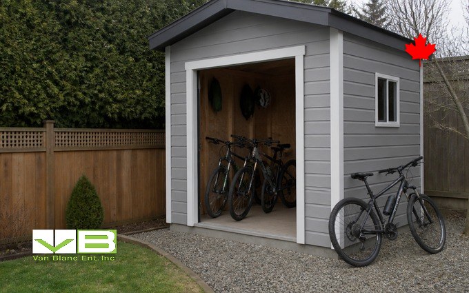 A grey backyard bike shed with the door open, bikes racked inside and one leaning outside on the gravel