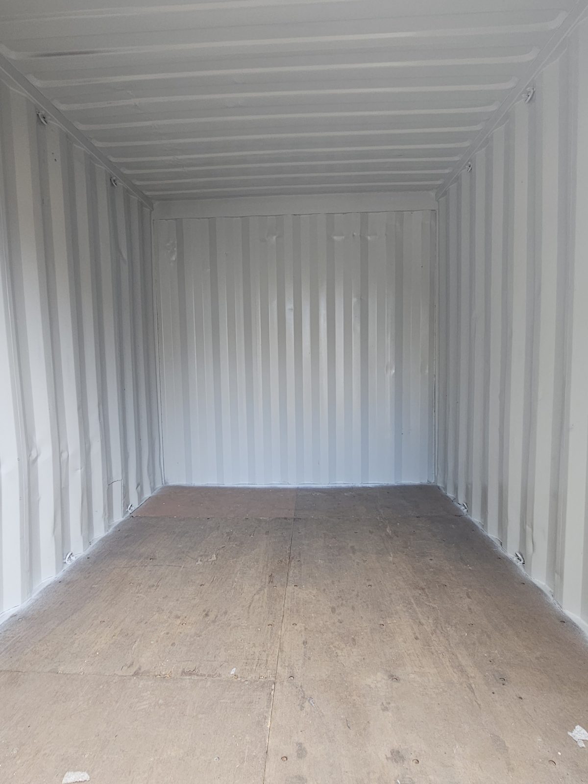Looking into the charcoal 10ft: white-painted corrugated walls and ceiling over a plywood floor, empty to the far end wall